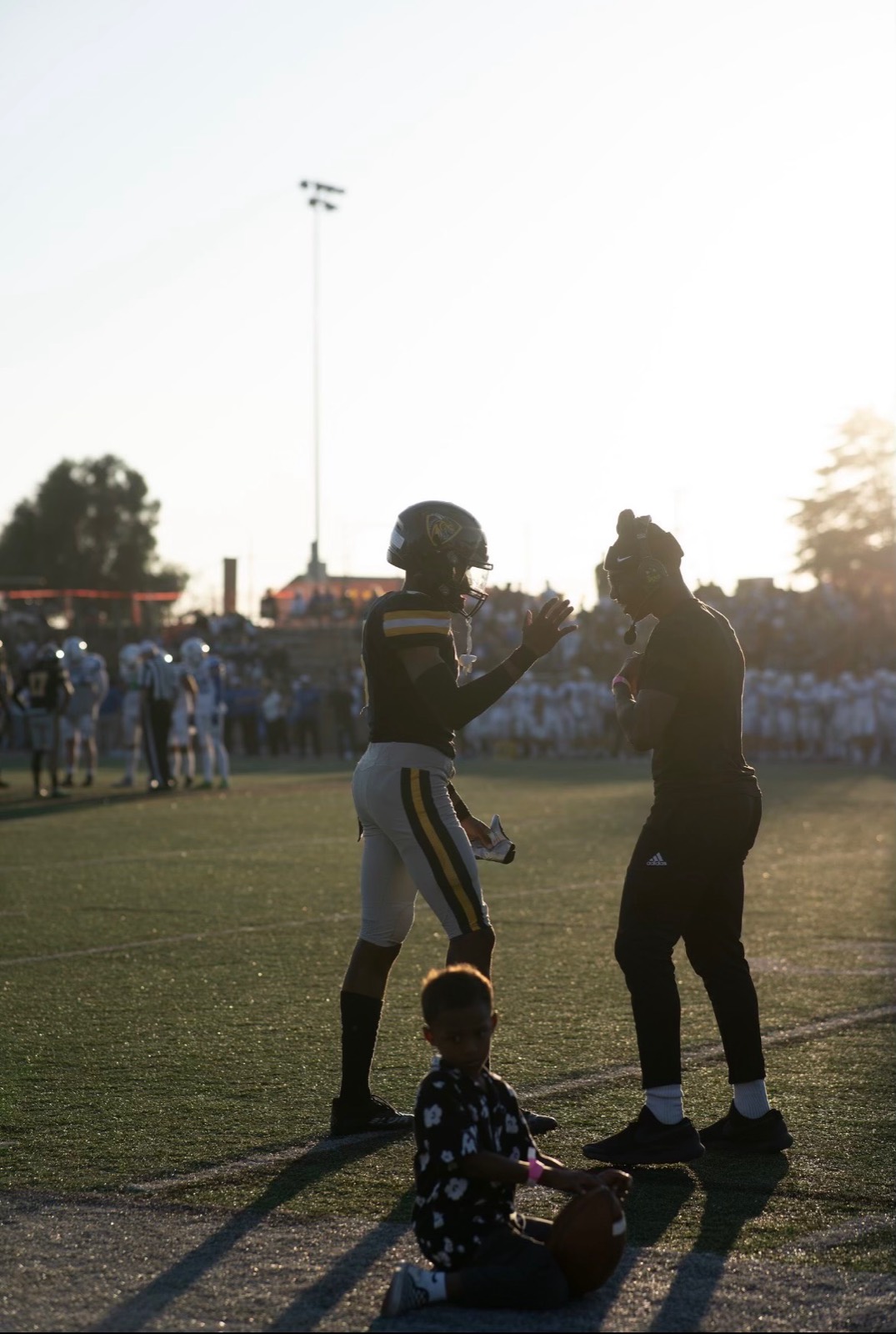 Coach Trammell talking with an athlete on the sideline at sunset
